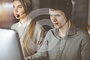 Businessman talking by headset while sitting in sunny office. Telemarketing concept