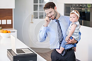 Businessman talking on mobile phone while carrying daughter