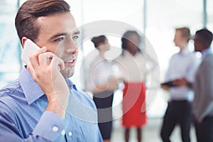 Businessman talking on mobile phone with colleagues discussing in background