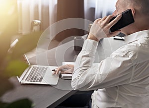 Businessman talking on mobile phone while looking at laptop screen. Business call in office