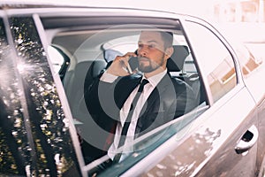 Businessman talking on the mobile phone and looking outside the window while sitting on back seat of car. Male business executive