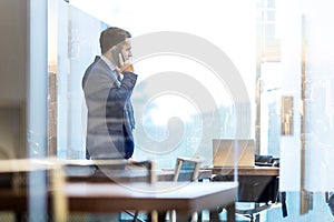 Businessman talking on a mobile phone while looking through window in NY