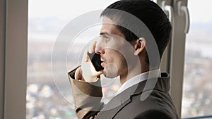 The businessman talking mobile phone near the panoramic window.