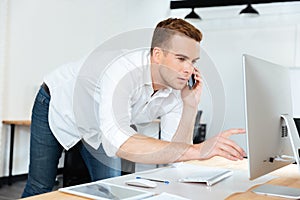 Businessman talking on mobile phone and using computer in office