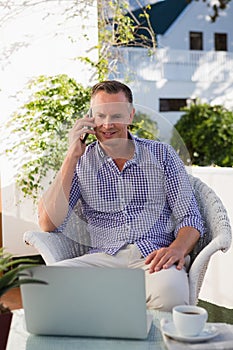 Businessman talking on mobile phone while using laptop in outdoors cafe