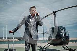 Businessman talking over the phone near private helicopter