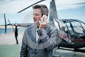 Businessman talking over the phone near private helicopter