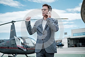 Businessman talking over the phone near private helicopter