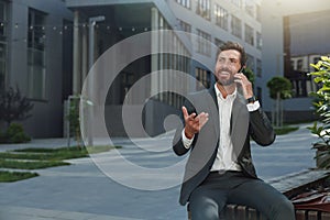 Businessman talking phone with client during break sitting near office building