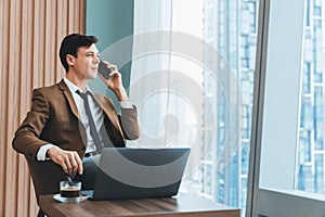 Businessman talking phone to manager while sitting near window. Ornamented.