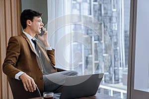 Businessman talking phone to manager while sitting near window. Ornamented.