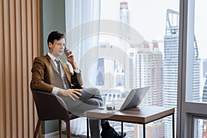 Businessman talking phone to manager while sitting near window. Ornamented.