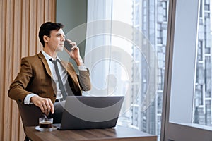 Businessman talking phone to manager while sitting near window. Ornamented.