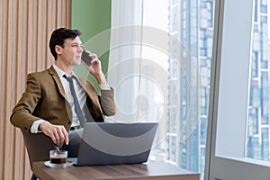 Businessman talking phone to manager while sitting near window. Ornamented.