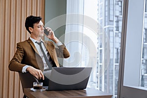 Businessman talking phone to manager while sitting near window. Ornamented.