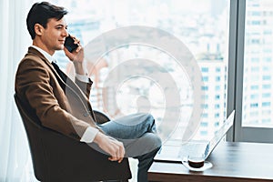 Businessman talking phone to manager while sitting near window. Ornamented.