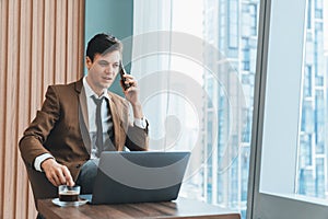 Businessman talking phone to manager while sitting near window. Ornamented.