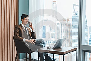 Businessman talking phone to manager while sitting near window. Ornamented.