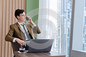 Businessman talking phone to manager while sitting near window. Ornamented.