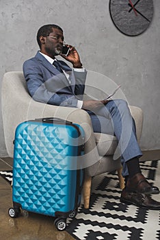 Businessman talking by smartphone and sitting in armchair travel bag