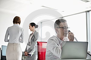 Businessman talking on telephone with colleagues in background at office