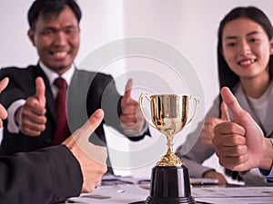 Businessman with teamwork in goal and successful showing trophy and thumb up rewarded for in the office