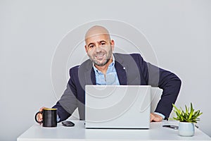 Businessman teleworking with a laptop having a coffee. Bald man