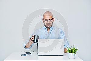 Businessman teleworking with a laptop having a coffee. Bald man with glasses