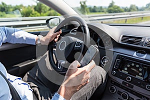 Businessman texting on his mobile phone while driving.