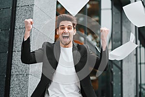 Businessman throwing papers documents into air and celebrates success on office building background. Freedom, successful