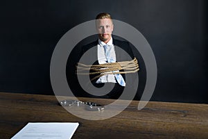 Businessman tied with rope sitting in front of table
