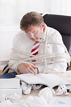 Businessman tied up with rope in the office. Work without end