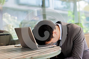 Businessman tiring and sleeping on his laptop in outdoor scene