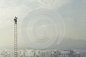 Businessman at the top of a long ladder observes the city with his binoculars