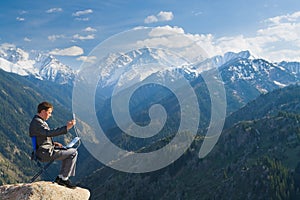 The businessman at the top of the mountain using wireless network with his laptop