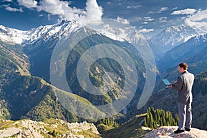 The businessman at the top of the mountain using wireless network with his laptop