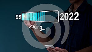 A businessman touches a virtual download bar with a loading progress bar on New Year's Eve, turning the year 2021 to 2022