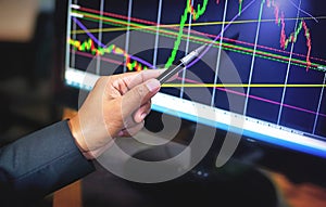 Businessman Trader hand point pen on chart trading screen to analyze market trends