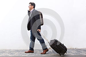 Businessman traveling with his suitcase and talking on cell phone outdoors