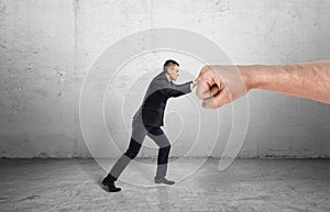 Businessman trying to resist huge male fist and move it away on grey background