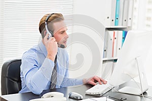 Businessman typing at computer while speaking with headset