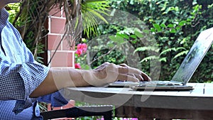 Businessman typing on the keyboard of his computer laptop at home. Patio. Garden view.