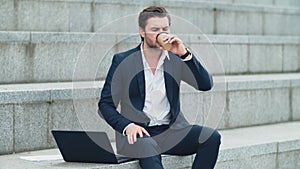 Businessman typing on laptop computer on street. Man drinking take away coffee