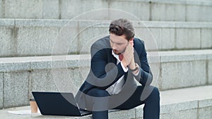 Businessman typing on laptop at street. Man in suit working outside office