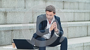 Businessman typing on laptop at street. Man in suit working outside office