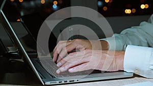 Businessman typing text or coding on laptop keyboard with hands in evening, closeup
