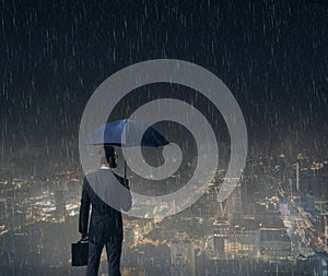 Businessman with umbrella standing over night city background.