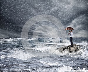 Businessman with umbrella during storm in the sea. Concept of insurance protection