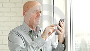 Businessman with unbound tie text using cellphone in front of office window