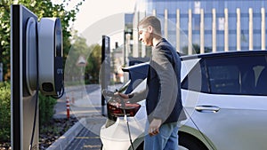 Businessman unplugging electric car. Luxury electrical car full. Electrical power filling compete and cable disconnected